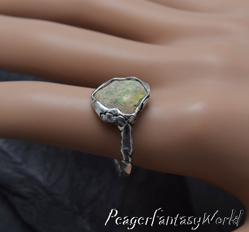 May include: A silver ring with a unique, irregular shaped opal gemstone set in a textured silver band. The opal has a milky white base with flashes of green and blue.