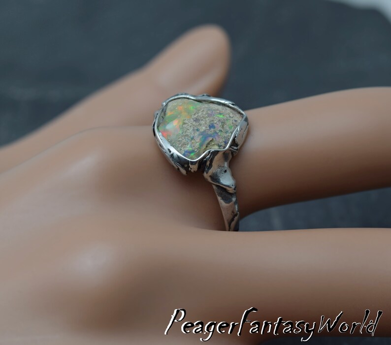 May include: A silver ring with a large, irregular shaped opal gemstone set in a textured silver band.