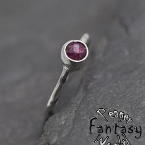 Puede incluir: Un anillo de plata con una pequeña piedra preciosa redonda de color rosa engastada en un engaste de bisel.