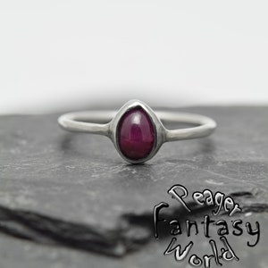 May include: A silver ring with a teardrop-shaped, deep red gemstone set in the centre.