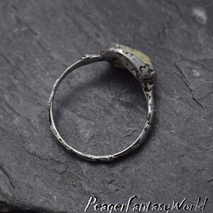 May include: A silver ring with a textured band and a green and white stone set in the top. The stone is oval shaped and has a rough, natural look.