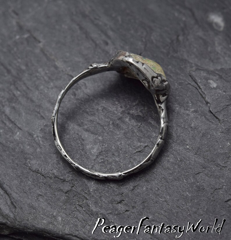 May include: A silver ring with a textured band and a green and white stone set in the top. The stone is oval shaped and has a rough, natural look.