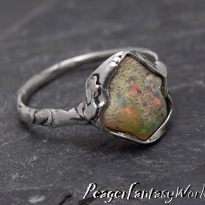 May include: A silver ring with a textured band and a large, irregular-shaped opal gemstone set in a silver bezel. The opal has a milky white base with flashes of iridescent color.