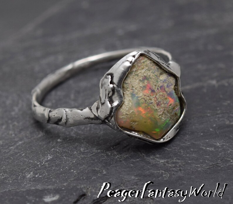 May include: A silver ring with a textured band and a large, irregular-shaped opal gemstone set in a silver bezel. The opal has a milky white base with flashes of iridescent color.