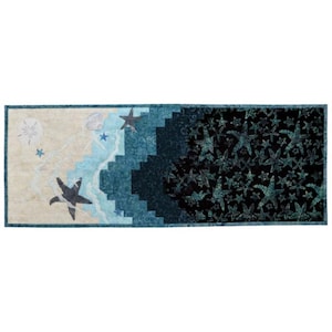 May include: A rectangular quilt with a beach scene on one side and a dark blue background with starfish on the other side. The beach side features a sandy beach with waves, seashells, and starfish. The dark blue side features a black background with a pattern of starfish in various shades of blue.
