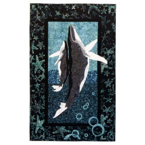 May include: A black and blue quilted wall hanging featuring two whales swimming upwards in a blue and white ocean scene with bubbles. The whales are silhouetted against a blue background with a black border of starfish.