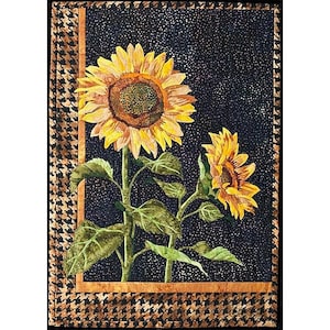 May include: Two sunflowers with yellow petals and brown centers are shown against a black background with a brown and black houndstooth border. The sunflowers are in bloom and have green leaves.