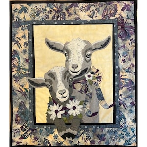 May include: Two gray and white goats with floral accents. The goat in the front is wearing a purple and green floral garland. The goat in the back is wearing a purple ribbon with a white flower.