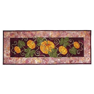 May include: A burgundy table runner with a decorative border featuring a repeating pattern of orange pumpkins and green leaves.