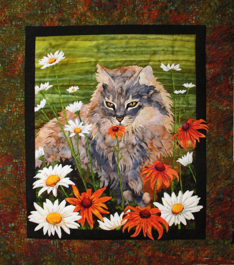 May include: A gray and white cat with long fur sits in a field of white daisies and orange flowers. The cat is looking directly at the viewer and has a flower in its mouth.