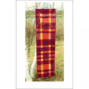 May include: A long, rectangular table runner with a plaid pattern in shades of red and orange. The runner is made of fabric and has a quilted texture.