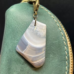 May include: A white and gray agate stone keychain with a brass clasp. The stone has a natural, organic shape and is attached to a brass chain.