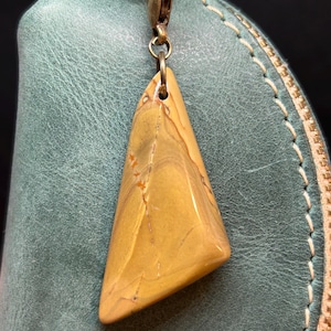 Puede incluir: Un llavero de metal dorado con un dije de piedra triangular de color marrón claro. La piedra tiene un patrón de mármol.