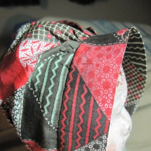 May include: A red, black, and white patterned fabric bonnet with a ruffled edge. The bonnet is made of a patchwork of different fabrics.