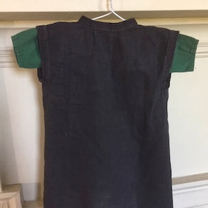 May include: A black linen tunic with short sleeves and a mandarin collar. The tunic is hanging on a hanger and has a green t-shirt underneath.