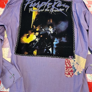 May include: Purple pinstripe button-down shirt with a large graphic on the back featuring the text "Purple Rain" and "Prince and the Revolution." The graphic shows a person on a motorcycle. Patches of fabric are sewn on the shirt.