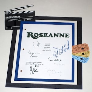 May include: A framed script from the TV show "Roseanne" with signatures from the cast members, including Roseanne Barr, John Goodman, Laurie Metcalf, Michael Fishman, and Sara Gilbert. The script is dated January 14, 1991. Three colorful "Admit One" tickets are also visible in the image.