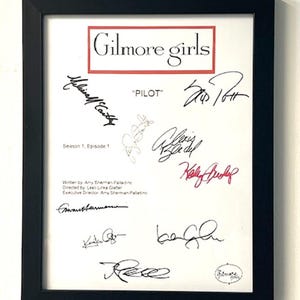 May include: A framed white sheet of paper with black text and signatures. The text reads "Gilmore Girls", "Pilot", "Season 1, Episode 1", "Written by Amy Sherman Paladino", "Directed by Lesli Linka Glater", and "Executive Director Amy Sherman Paladino".