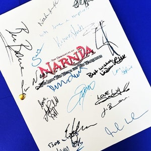 May include: A white script with the title "The Chronicles of Narnia: The Lion, the Witch and the Wardrobe" in red and black lettering. The script is signed by several people, including the actors who played the characters in the movie.