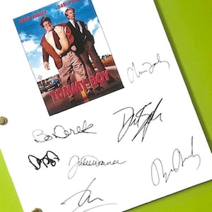 May include: A white sheet with a movie poster for "Tommy Boy" featuring Chris Farley and David Spade. The sheet is covered with multiple signatures in black ink, likely autographs. The background is a bright green surface.