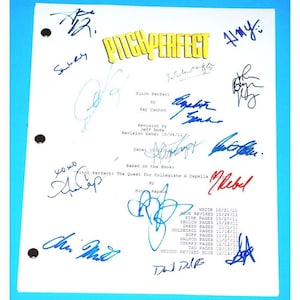 May include: A white sheet of paper with the title "Pitch Perfect" written in yellow letters. The paper is signed by multiple people, including the names "Rebel", "Jeff Roda", and "Ray Cannon".
