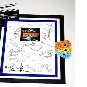 May include: A framed movie script for the film "Back to the Future" with multiple signatures from the cast and crew. The script is surrounded by a black and blue frame. Three movie ticket stubs are attached to the right side of the frame.