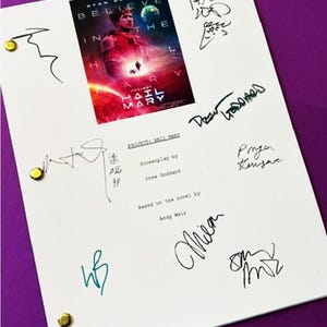 May include: A white screenplay cover for Project Hail Mary featuring a movie poster graphic with Ryan Gosling, multiple handwritten signatures in black and teal ink, and three gold-colored metal fasteners along the left edge of the document.