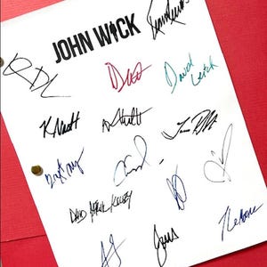 May include: A white sheet of paper with the title "JOHN WICK" written in black ink. The paper is covered in various signatures in blue, black, red, and green ink.