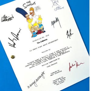 May include: A white paper with the title "The Simpsons" and character illustrations, including Bart Simpson. The script is signed by multiple individuals. The paper is on a blue surface.