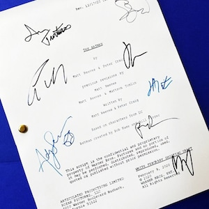 May include: A white script titled "THE BATMAN" with multiple signatures in blue and black ink. The script is on a blue surface and includes text about the film's creators and copyright information.