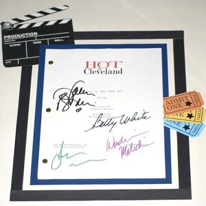 May include: A white script for the TV show "Hot in Cleveland" with signatures from the cast members, including Betty White,  and a clapperboard. The script is framed with a black and blue mat.