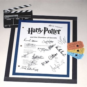 May include: A white framed document with a blue border, featuring the title "Harry Potter and the Chamber of Secrets" with multiple signatures. The document is accompanied by a black and white clapperboard and three colorful tickets with the text "ADMIT ONE" printed on them.