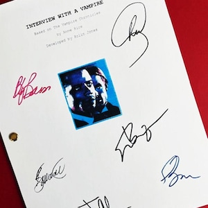 May include: A white script with the title "INTERVIEW WITH A VAMPIRE" and the text "Based on The Vampire Chronicles by Anne Rice Developed by Rolin Jones". The script is signed by six people in black, blue, and pink ink.