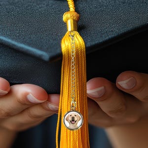 May include: A gold tassel charm with a small picture of a dog on it. The tassel is attached to a graduation cap.