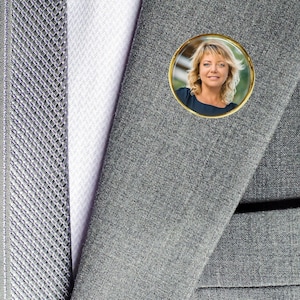 May include: A gray suit jacket with a small round pin featuring a woman with blonde hair.
