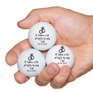 May include: Three white golf balls with black text and a ring design. The text reads "It takes a lot of balls to say "I do" 06.24.2023".