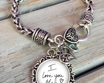 May include: Silver bracelet with a charm that says "I love you Mom" in handwritten script. The bracelet has a braided chain design and a heart-shaped clasp.