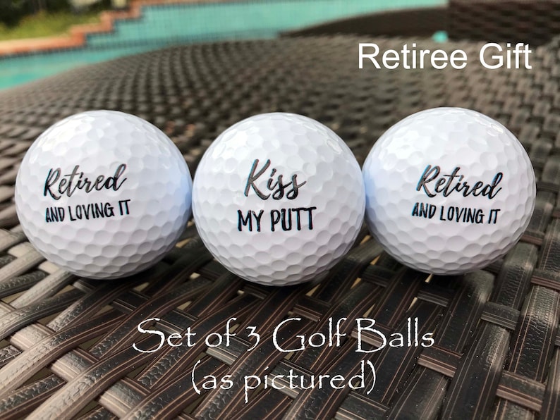 May include: Set of three white golf balls with black lettering. The golf balls say "Retired and Loving It", "Kiss My Putt", and "Retired and Loving It".