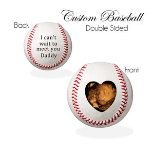 May include: A white baseball with red stitching. One side has the text "I can't wait to meet you Daddy". The other side has a heart-shaped cutout with a sonogram image inside.
