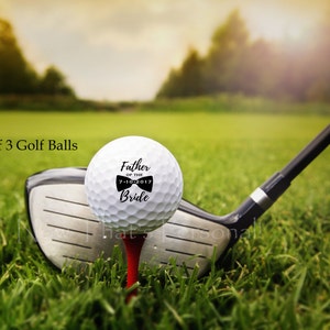 May include: Set of three white golf balls with black text and a bow tie design. The text reads "Father of the Bride" with the date "7-10-2017".