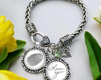 May include: A silver bracelet with a fingerprint charm, a heart charm, and a charm with the handwritten text "Love you".