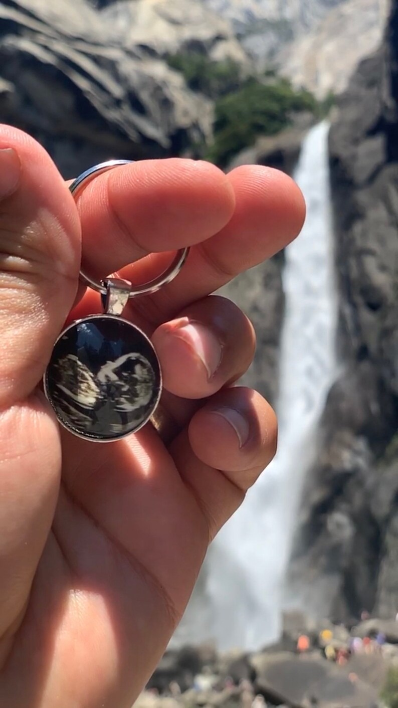 以下が含まれることがあります： 黒と白の超音波画像が写った丸い透明なチャームが付いたシルバーのキーホルダーです。