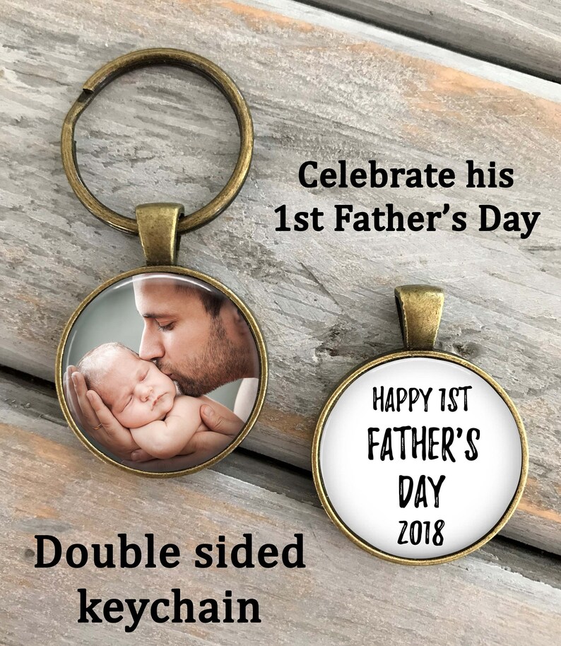 May include: Double-sided keychain with a photo of a father kissing a baby on one side and the text "Happy 1st Father's Day 2018" on the other side.