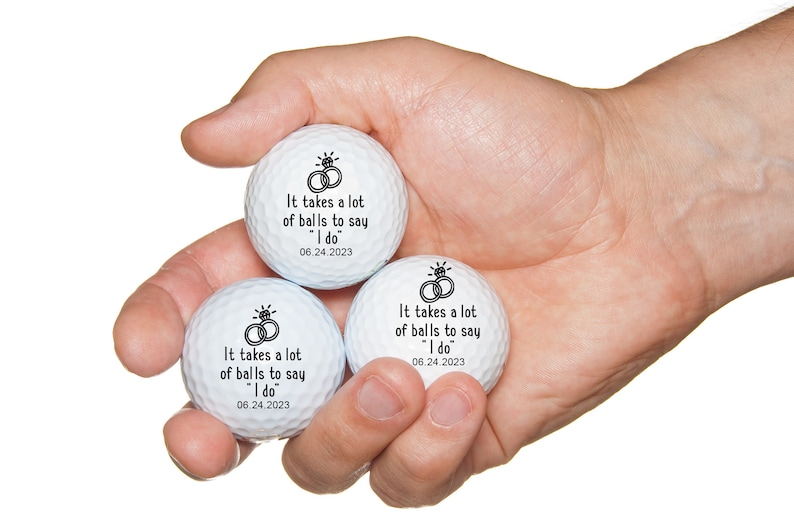 May include: Three white golf balls with black text and a ring design. The text reads "It takes a lot of balls to say "I do" 06.24.2023".