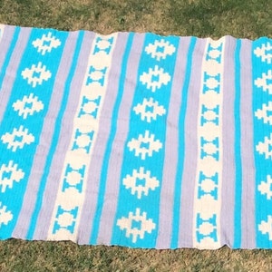 May include: A blue and white striped throw blanket with a geometric pattern. The blanket is made of a soft, woven fabric and has a fringed edge.