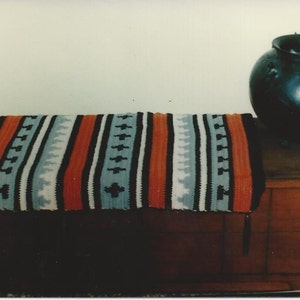May include: A wooden chest with a colorful striped blanket on top. A black ceramic pot sits on the chest.