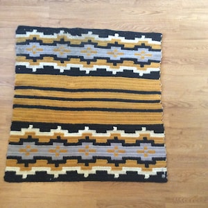 May include: A crocheted rug with a geometric pattern in shades of black, white, gray, and mustard yellow.