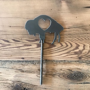 May include: A metal silhouette of a buffalo with a heart cut out of its center. The buffalo is attached to a metal rod.