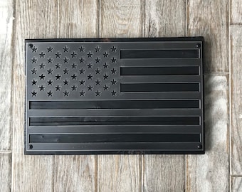 May include: A black metal American flag wall decor with a distressed finish. The flag is made of metal and has a rustic look. The stars and stripes are cut out of the metal, creating a unique and eye-catching design.