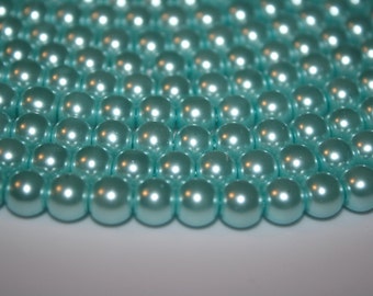 May include: A close-up of a large quantity of light blue pearl beads. The beads are arranged in a circular pattern, creating a shimmering effect.